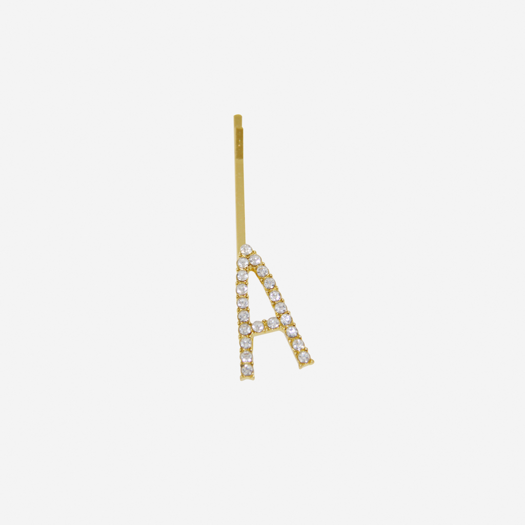 Gold and crystal hair slide featuring the letter 'C' on an off white background