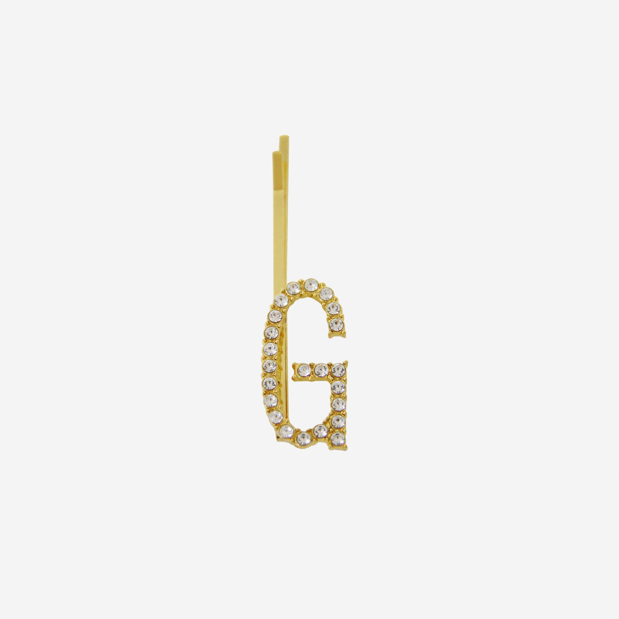 Gold and crystal hair slide featuring the letter 'G' on an off white background