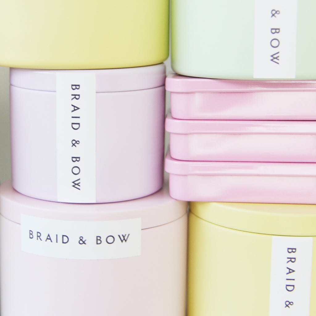 Pastel-colored tins with 'Braid & Bow' branding 