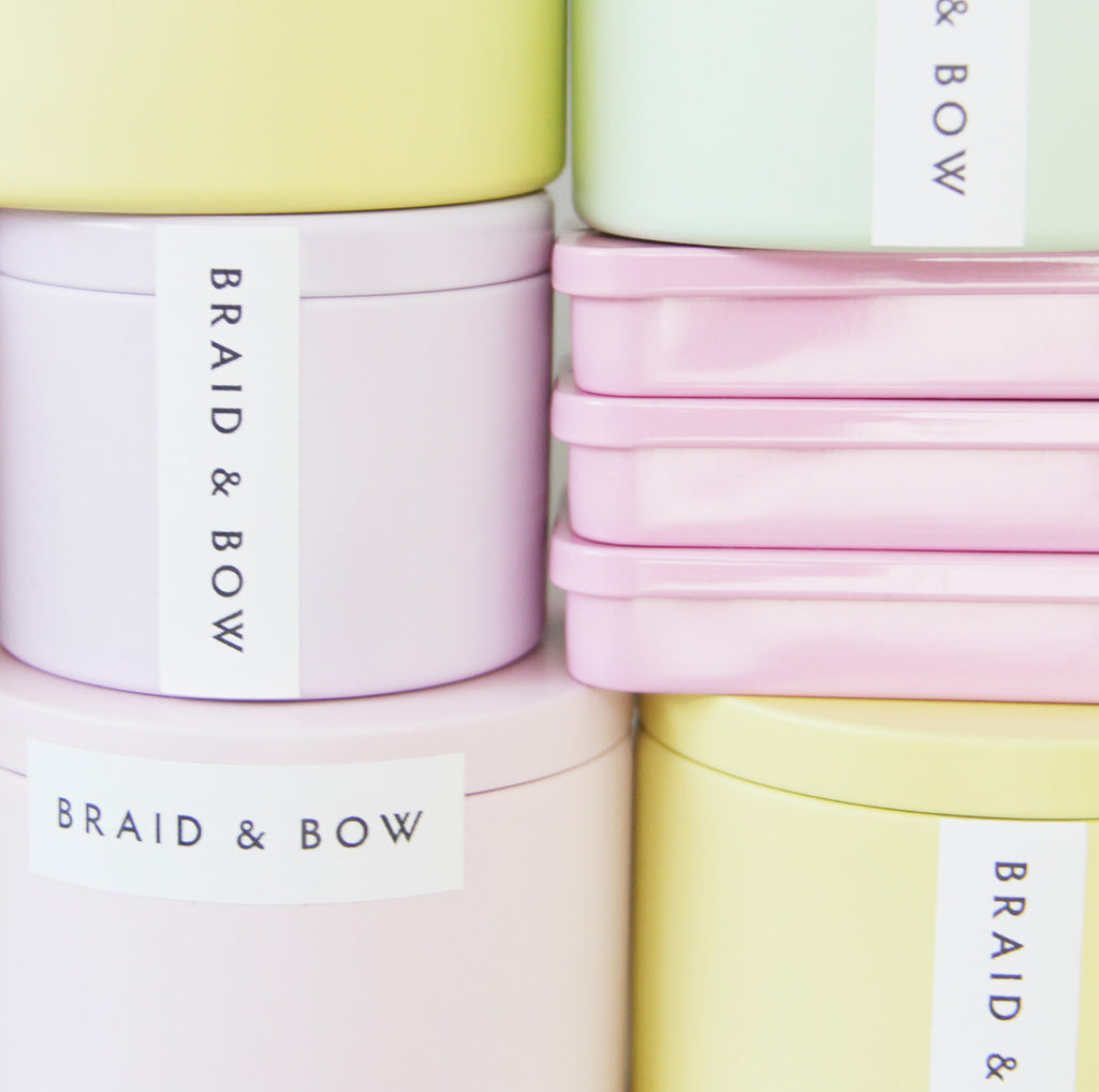Pastel-colored tins with 'Braid & Bow' branding on a white background