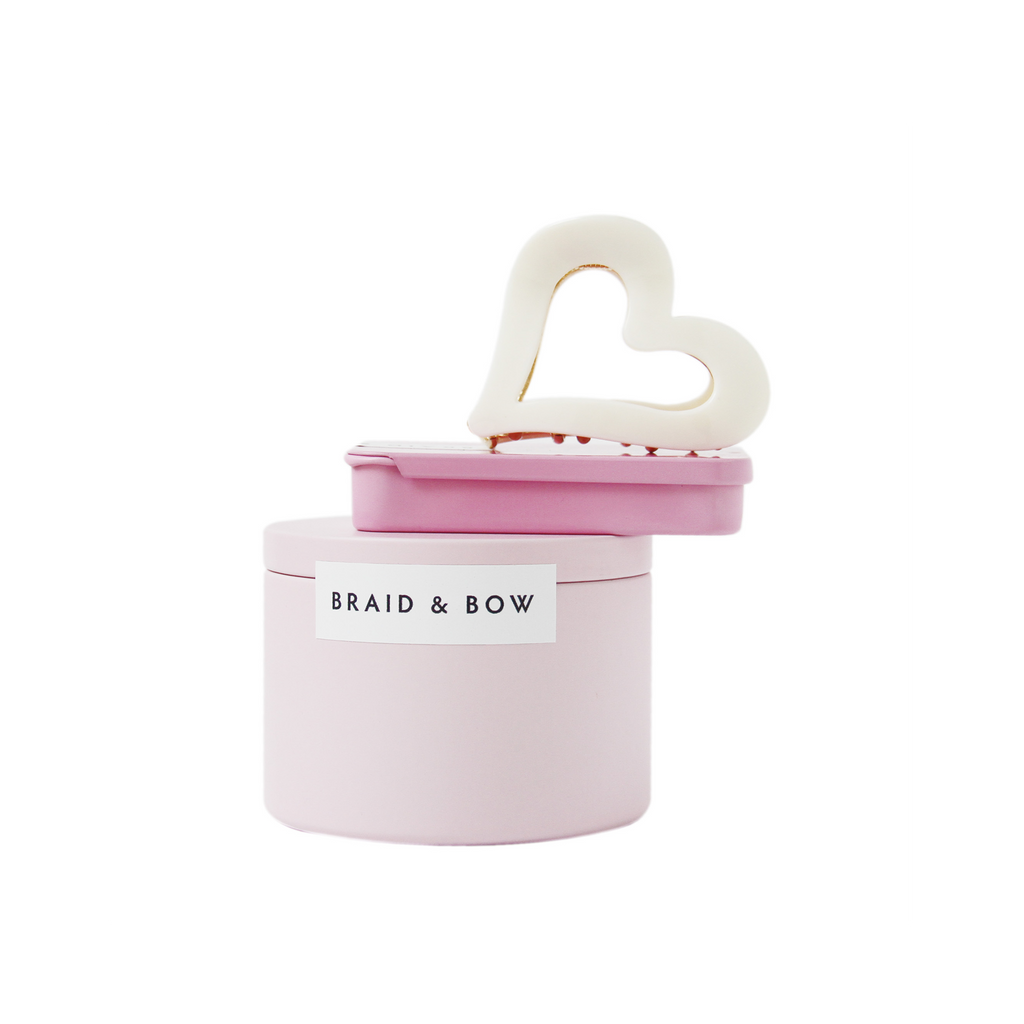 Braid & Bow gift set, showing a stack of tins containing silk scrunchies and non crease hair clips with a cream heart hair claw balanced on top, on a white background