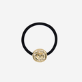 Black hair elastic with a gold and pearl vintage inspired button, on an off white background