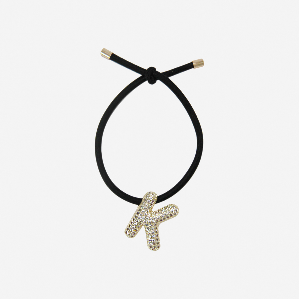Black hair tie with gold letter 'K' charm on an off white background