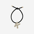 Black hair tie with gold letter 'K' charm on an off white background