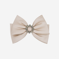 Taupe bow hair clip with a decorative crystal center on an off white background