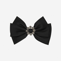 Black bow hair clip with a decorative crystal center on an off white background