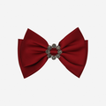 Red bow hair clip with a decorative crystal center on an off white background