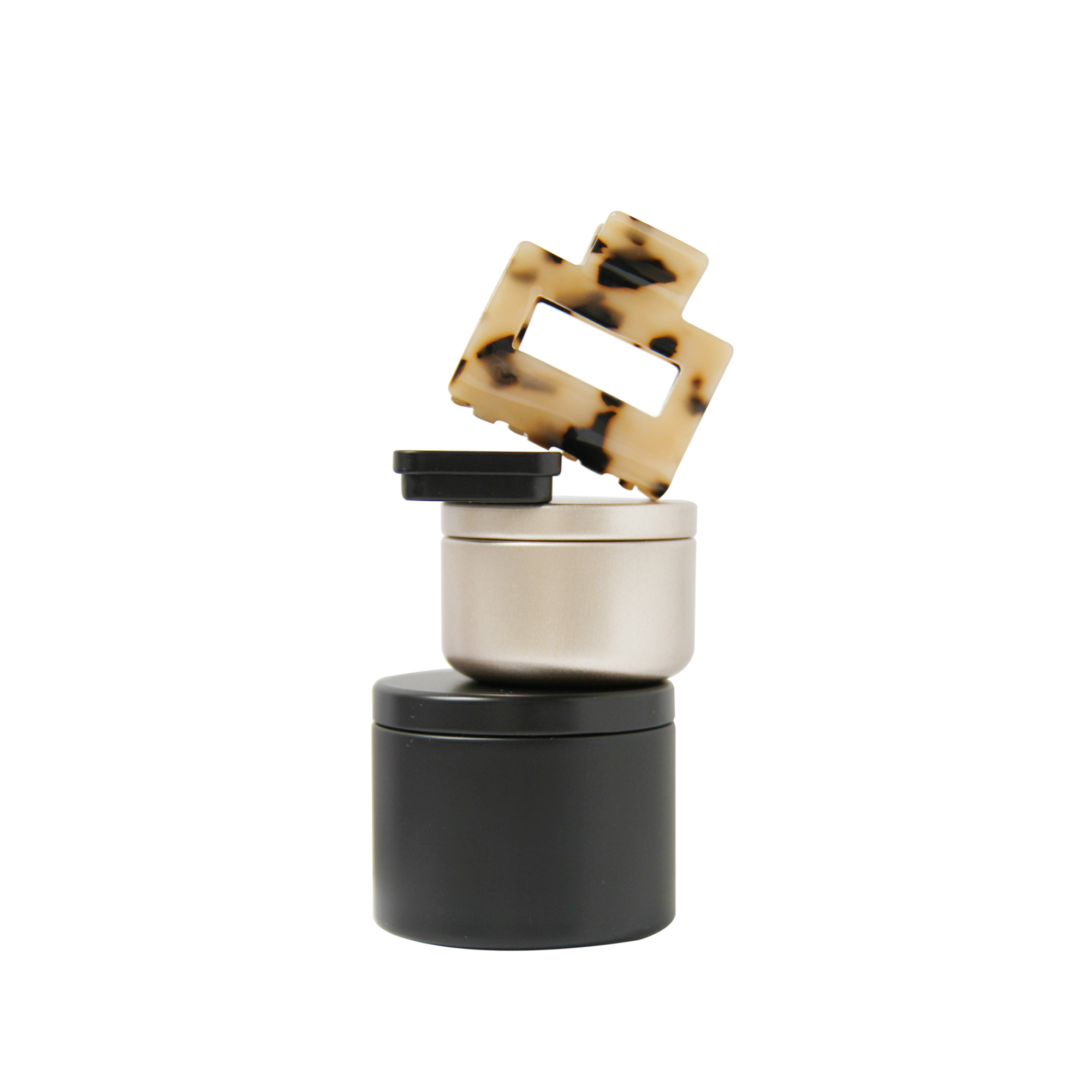 Braid & Bow gift set, stack of black and gold tins containing hair claws, hair ties and kirby grips with a tortoiseshell hair claw balanced on top, on a white background