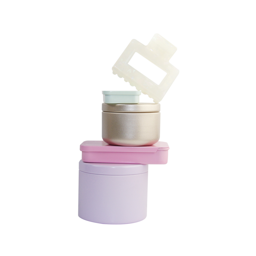 Braid & Bow gift set, stack of colourful tins containing hair claws, hair ties and kirby grips with a hair claw balanced on top, on a white background