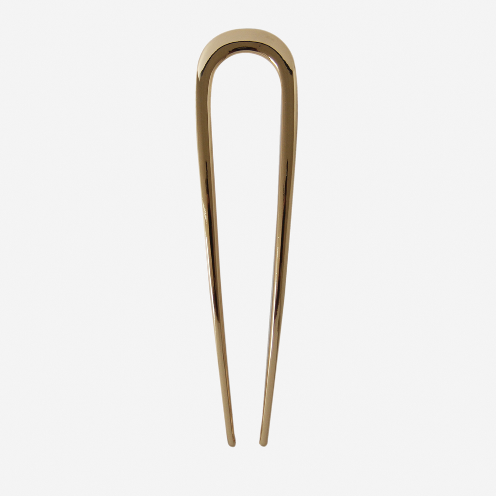 Gold metal french hair pin on an off white background