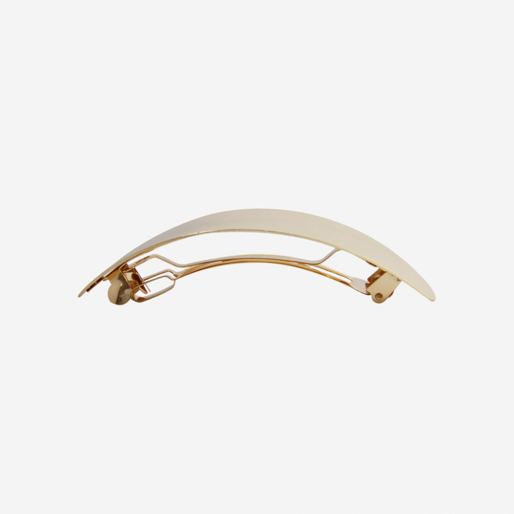Oval gold slightly curved hair clip, side view showing the hair barrette fastening, on an off white background