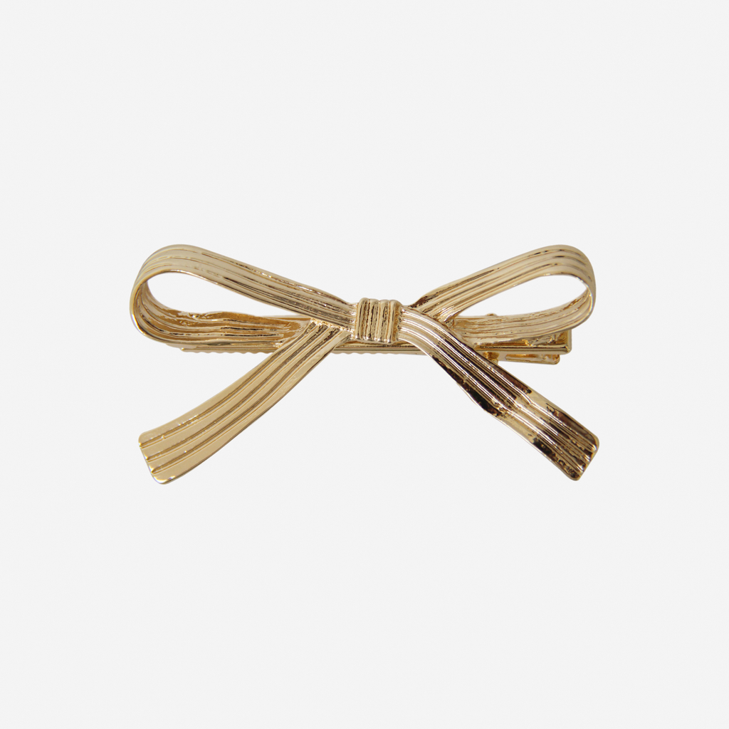 Gold ribbon bow hair clip on an off white background