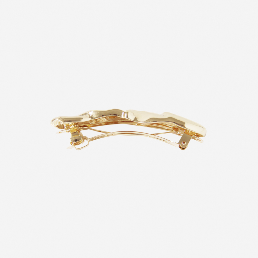 Gold folded hair clip, side view showing the barrette fastening, on an off white background