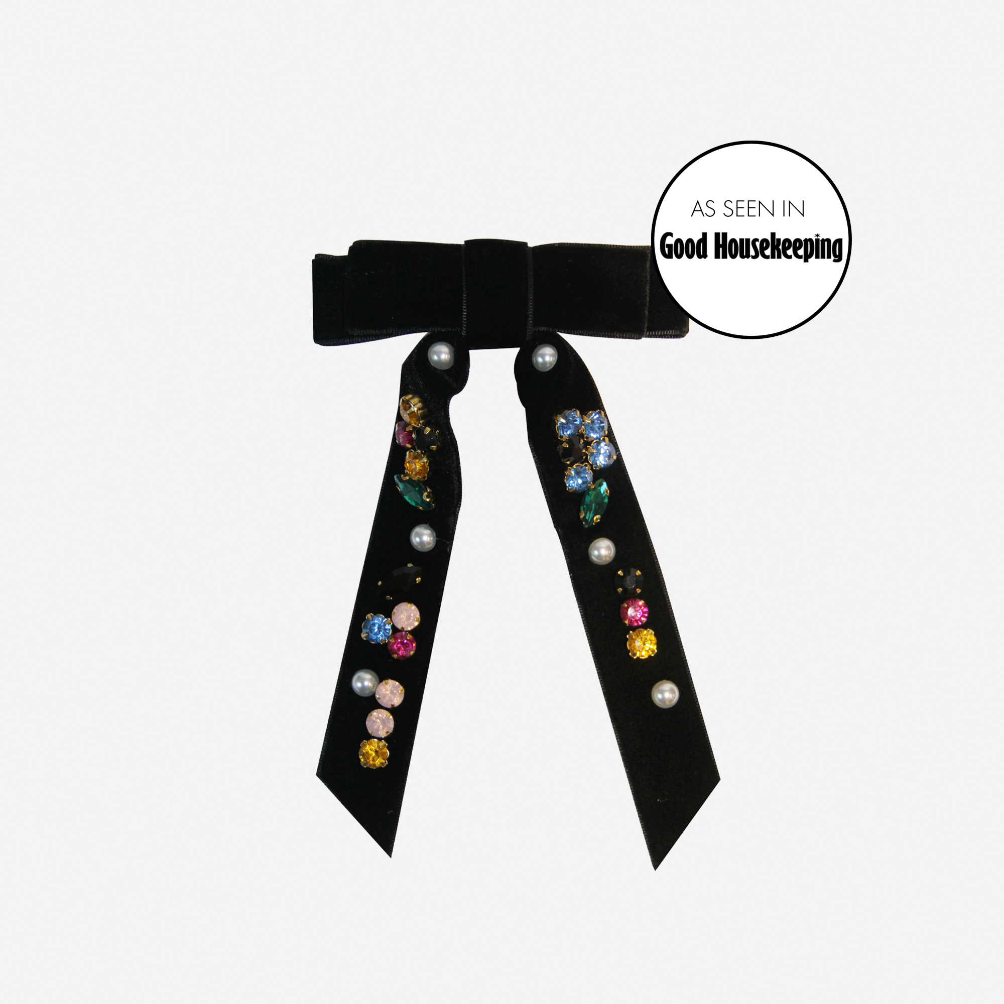 Black velvet hair bow that embellished with colourful jewels and pearls on an off white background
