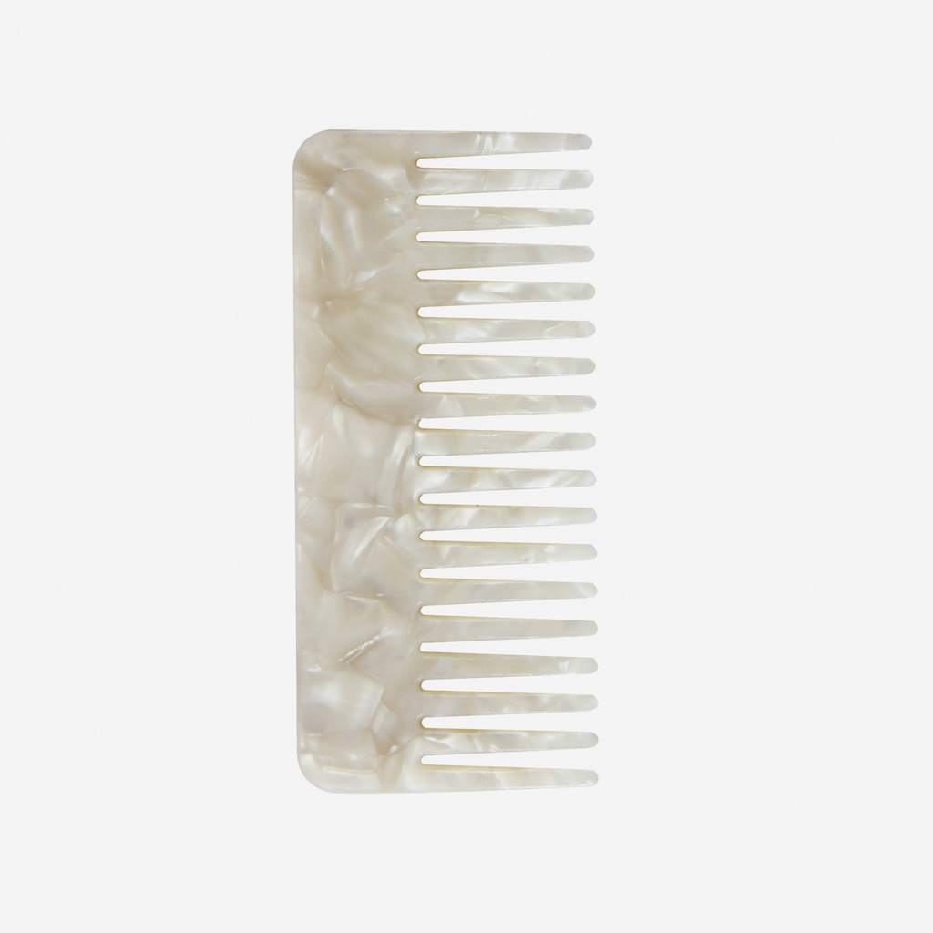 Wide tooth mother of pearl resin hair comb on an off white background
