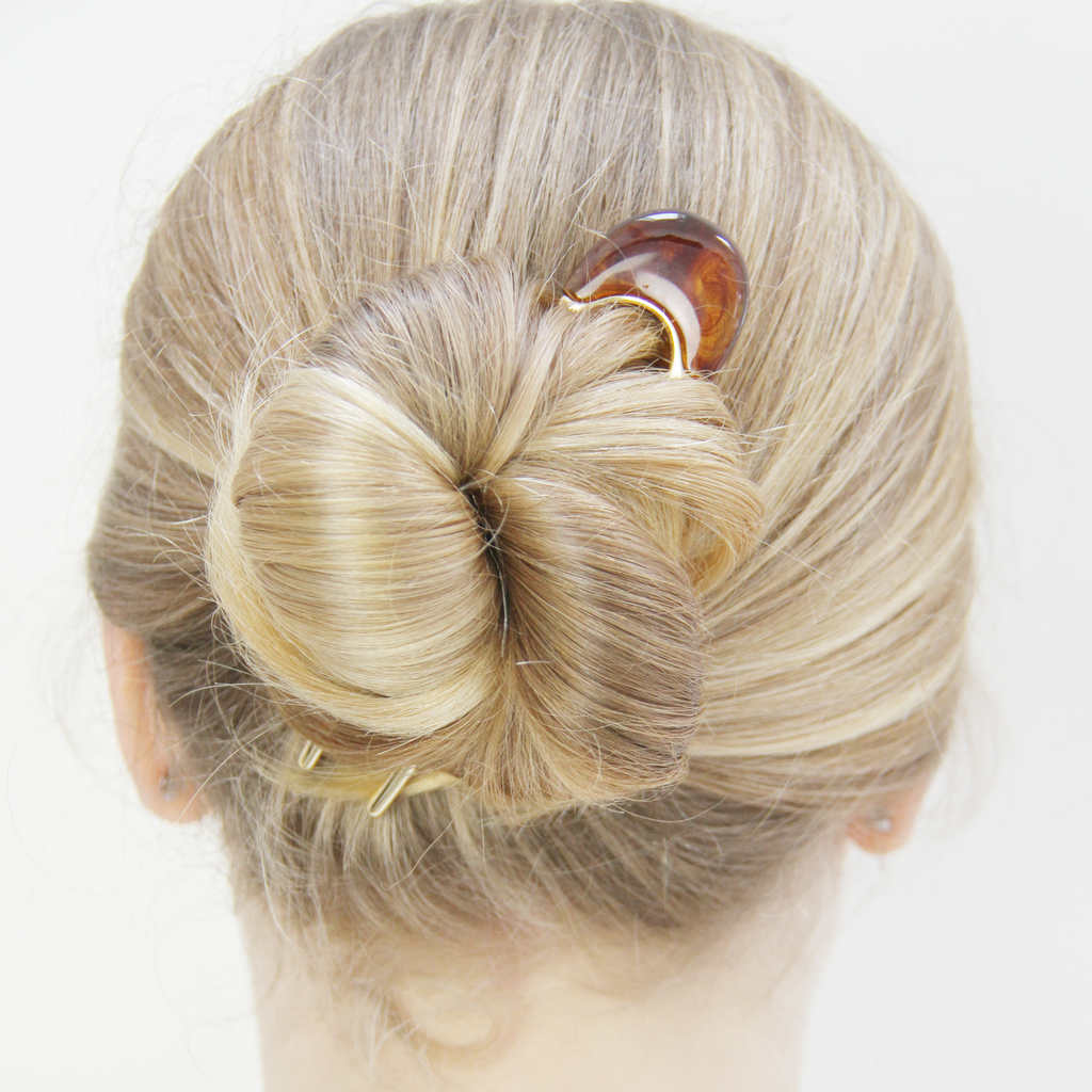 Model with a blonde bun that's being help in place with a gold and brown resin hair pin.