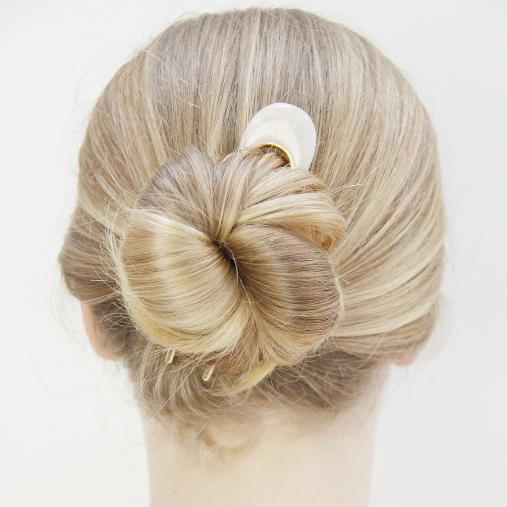 Model with a blonde bun that's being help in place with a gold and cream resin hair pin.