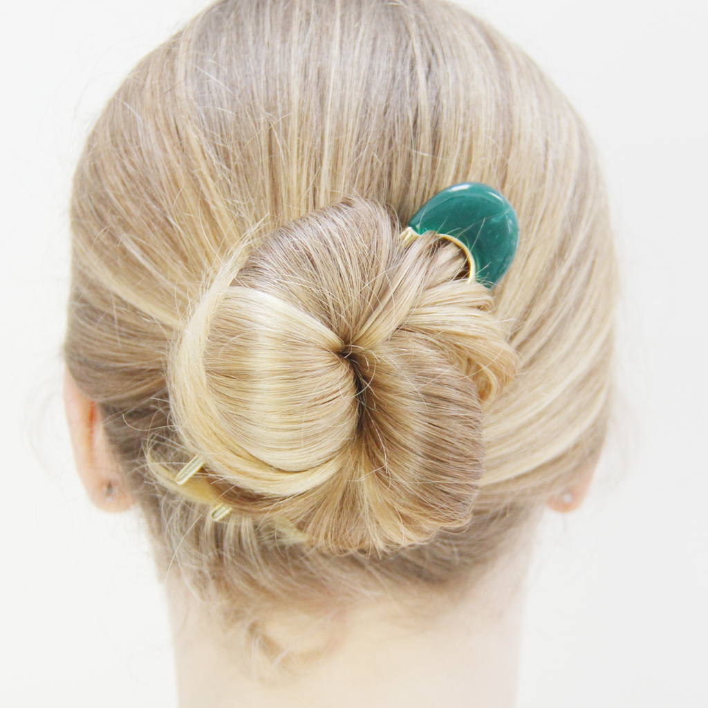 Model with a blonde bun that's being help in place with a gold and green resin hair pin.