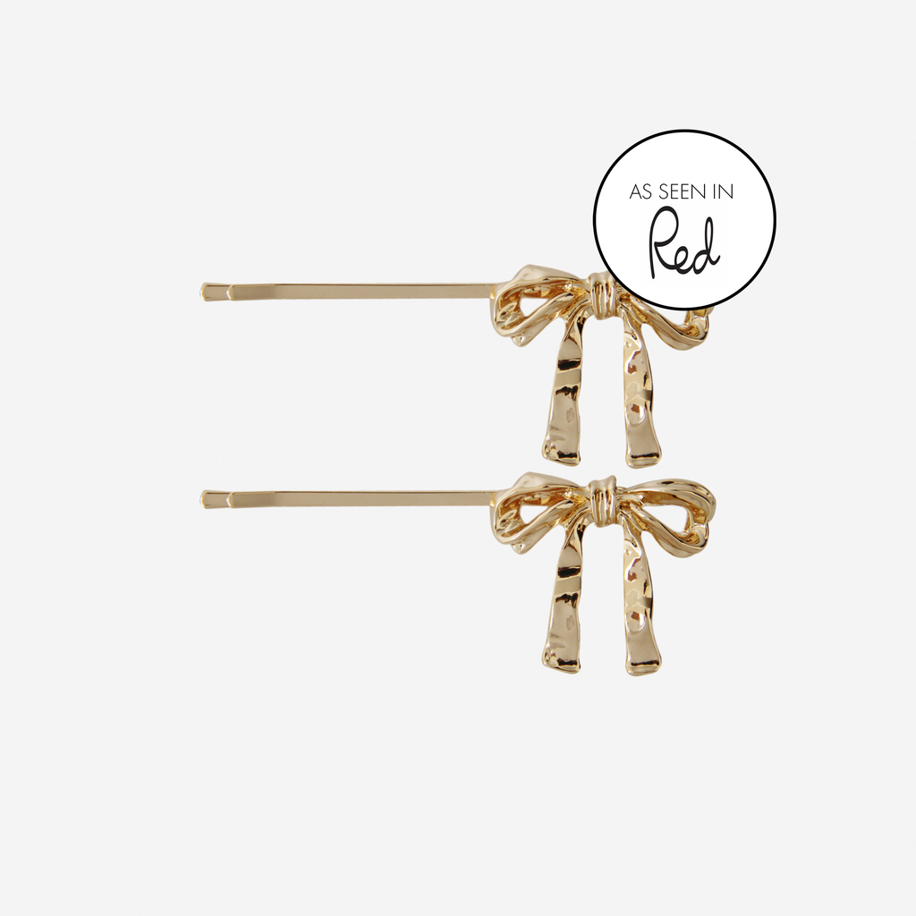 Set of 2 gold bow hair slides, featuring an as seen in red magazine logo, on an off white background