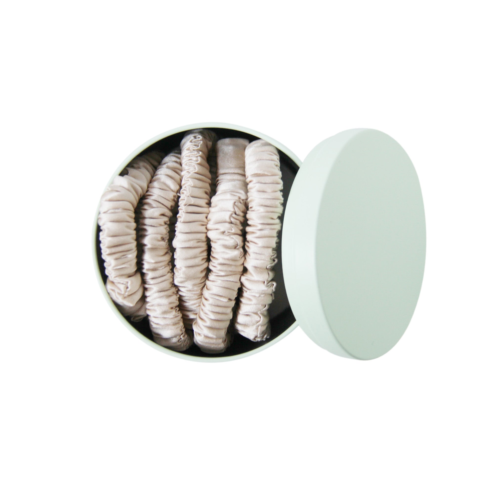 Set of 5 champagne silk hair ties in a green tin on a white background