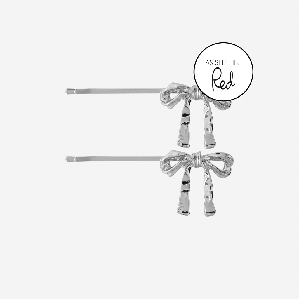 Set of 2 silver bow hair slides, featuring an as seen in red magazine logo, on an off white background