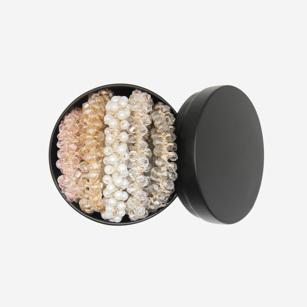 Set of 5 beaded hair ties, in 5 different colours - pink, topaz, crystal, smokey quartz and pear, in a black tin on an off white background