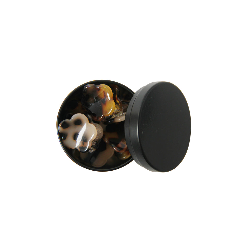 set of six tortoiseshell hair claws in a open black tin on a white background