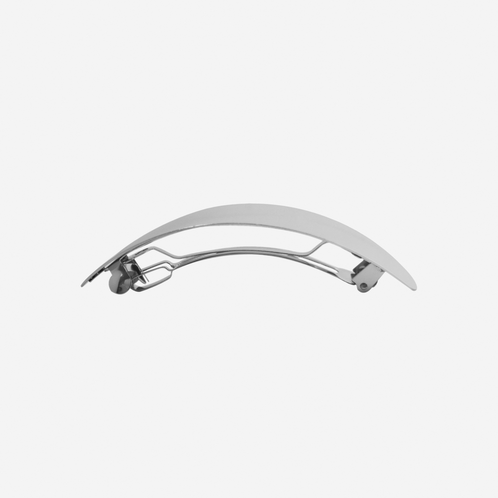 Oval silver slightly curved hair clip, side view showing the hair barrette fastening, on an off white background