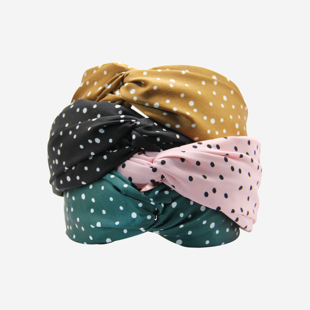Set of four polka dot headbands in black, pink, green, and braonze on an off white background
