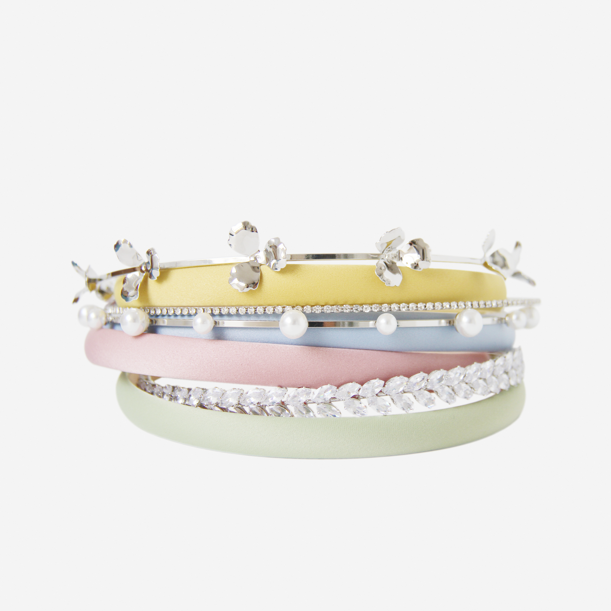 Stack of pastel coloured hairbands and crystal and pearl hairbands on an off white background