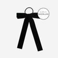 Black velvet bow hair tie on an off white background, featuring  as seen in'SheerLuxe' logo