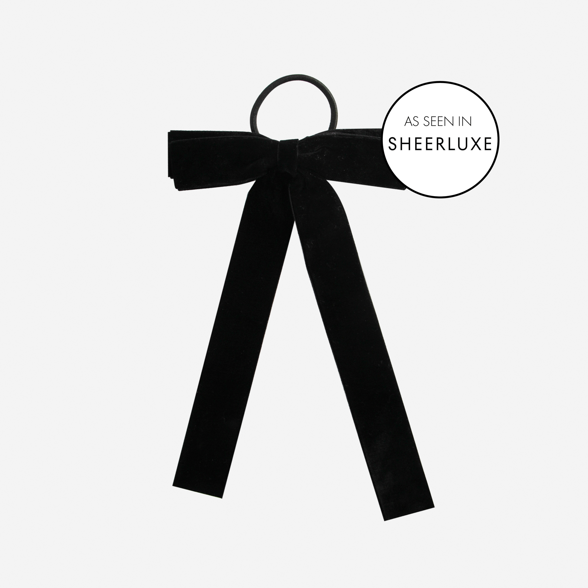 Black velvet bow hair tie on an off white background, featuring  as seen in'SheerLuxe' logo