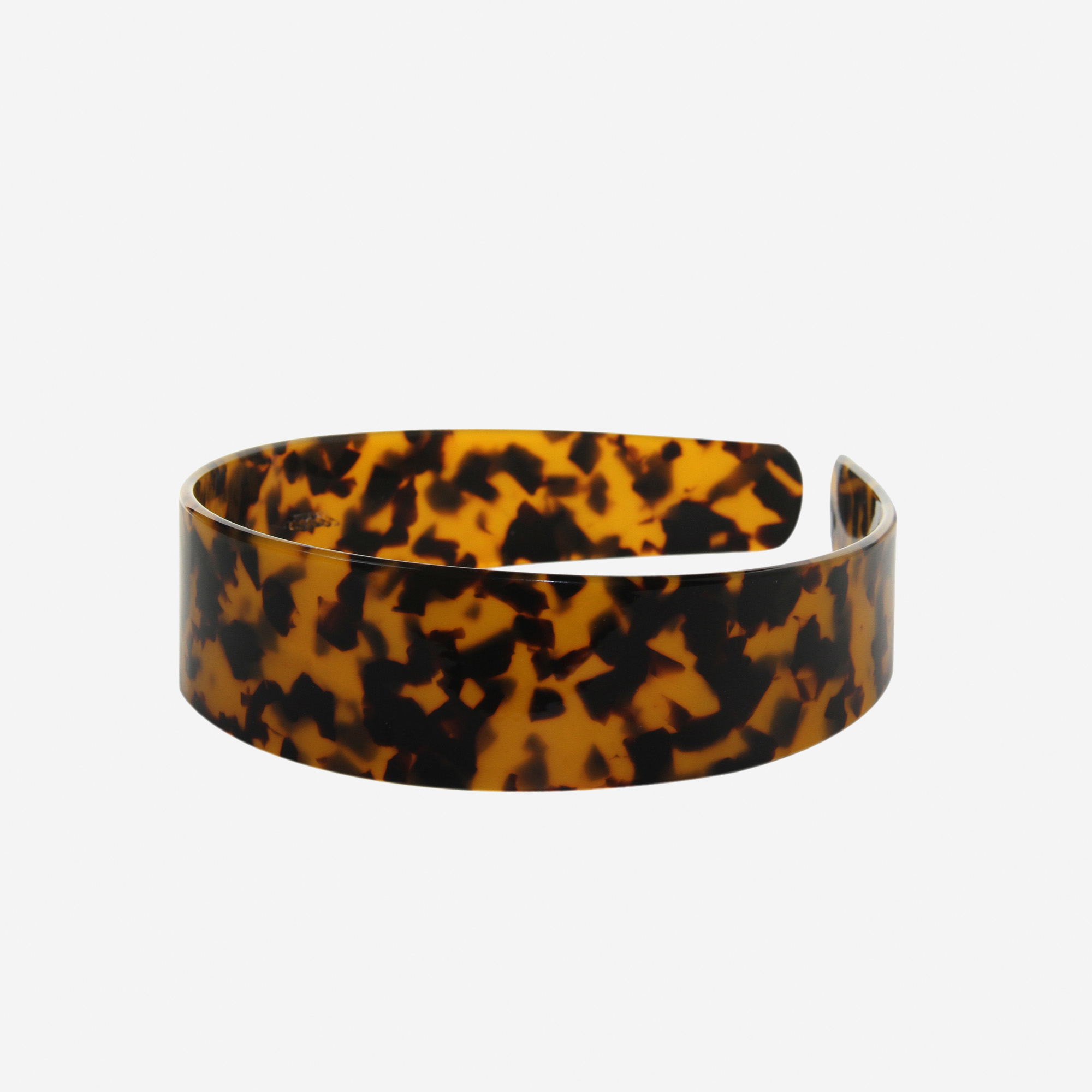 A glossy dark tortoiseshell resin hairband on a off white background