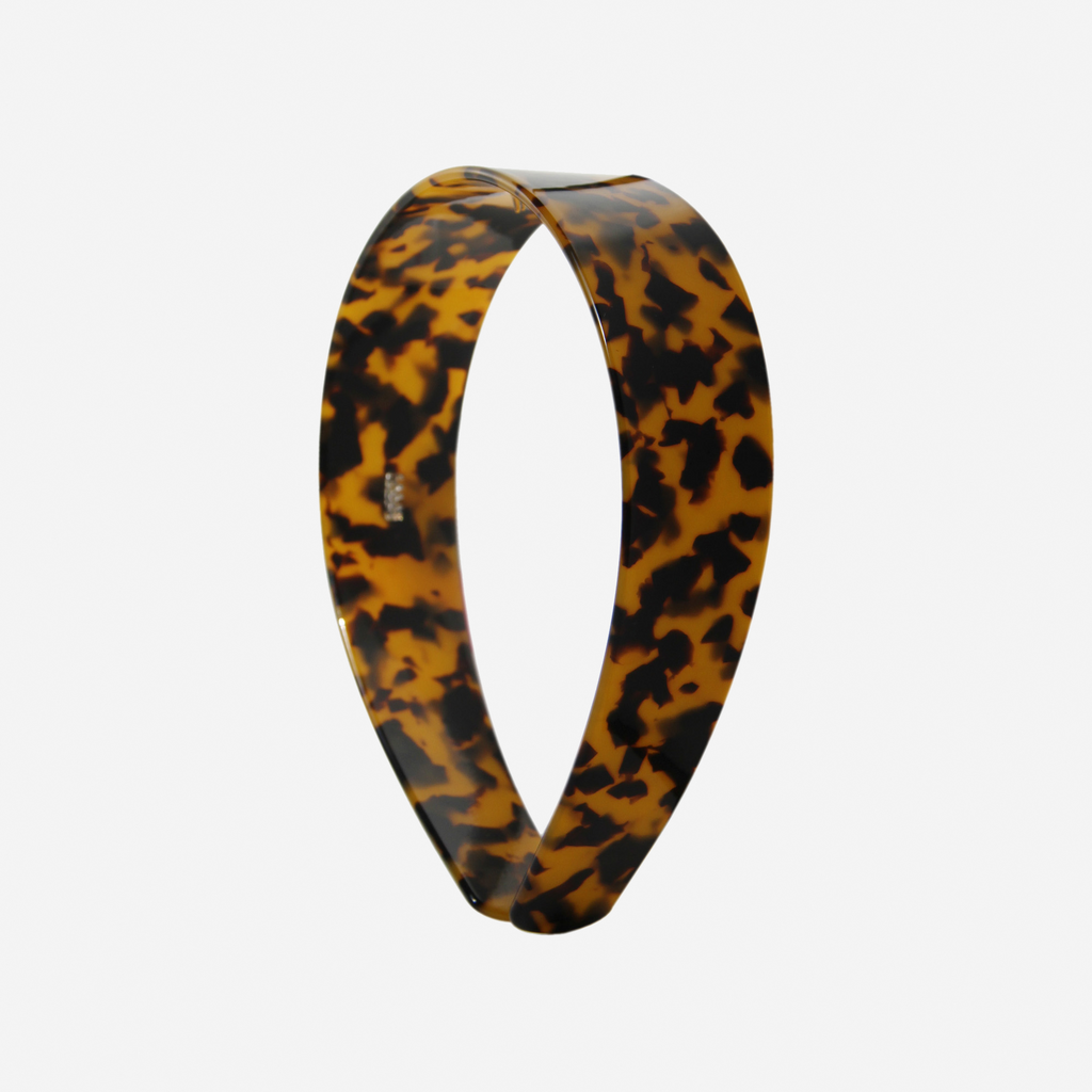 A glossy dark tortoiseshell resin hairband on a off white background