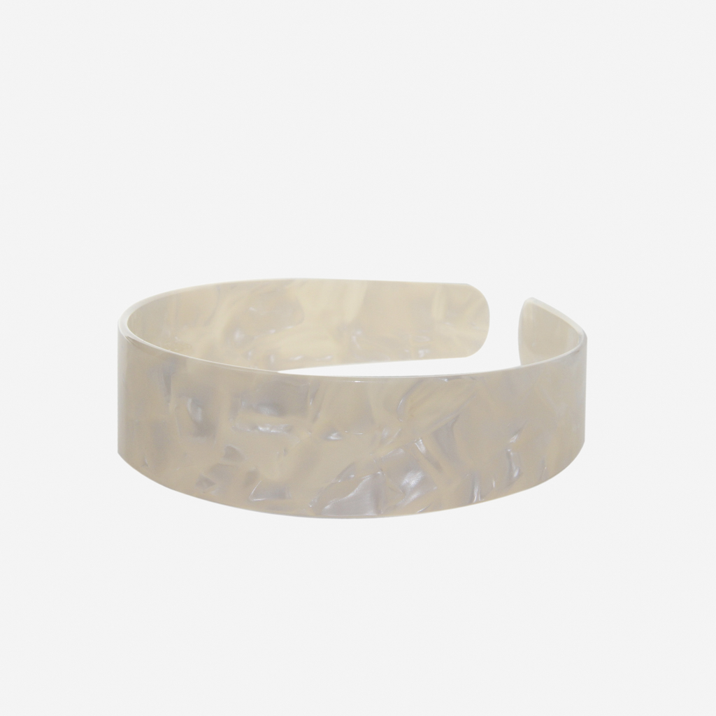 A glossy mother of pearl resin hairband on a off white background