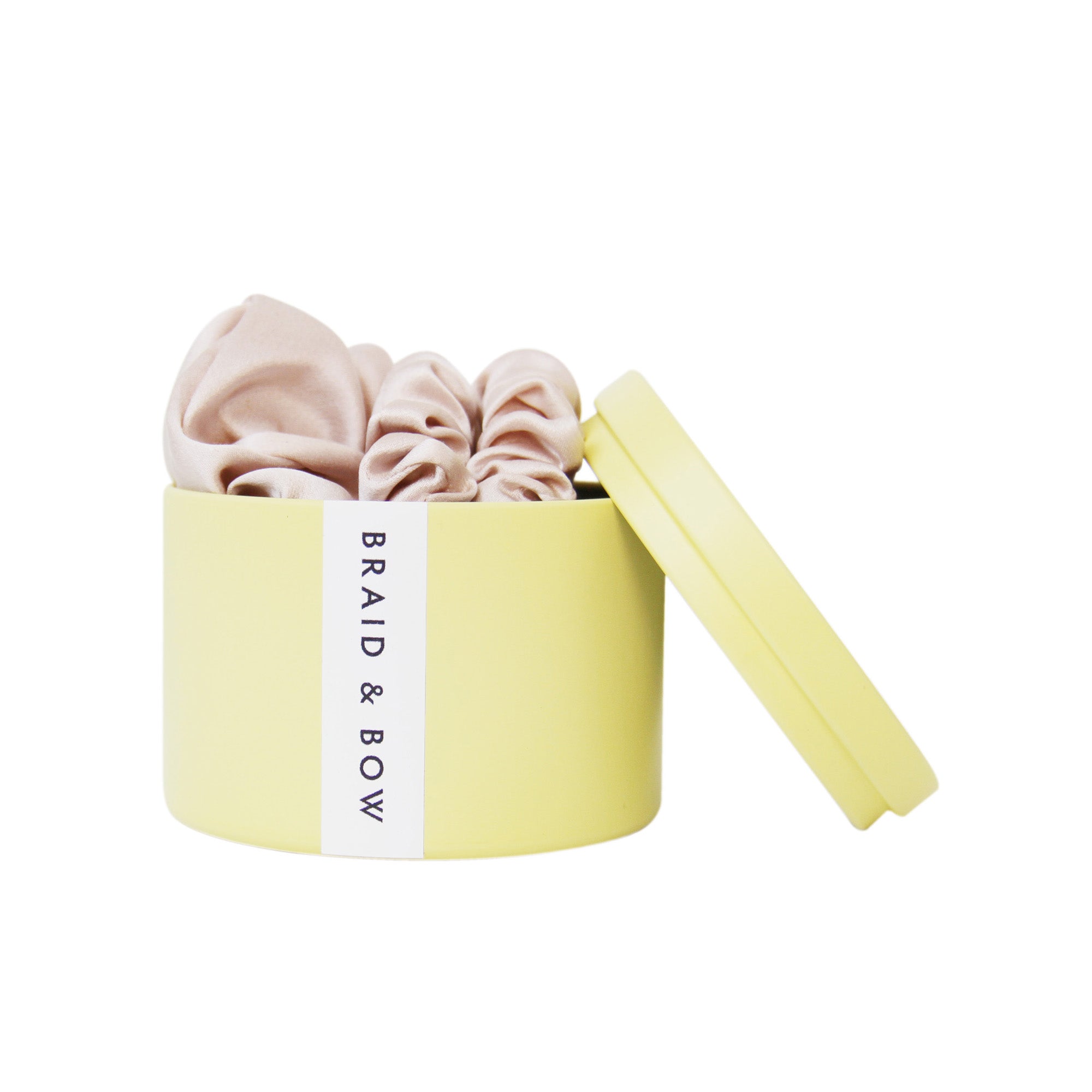 Yellow Braid & Bow tin with three blush silk scrunches on a white background